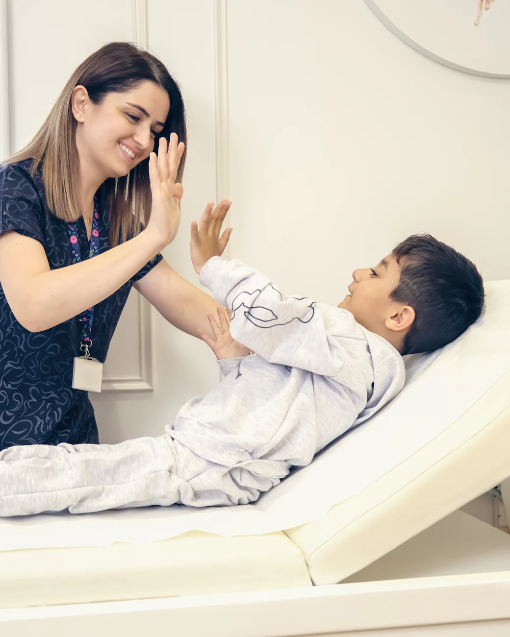 A nurse gives a smiling boy a high five on the exam table